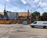 Roofing crew removing old shingles from a steep Minneapolis church roof beside the damaged steeple